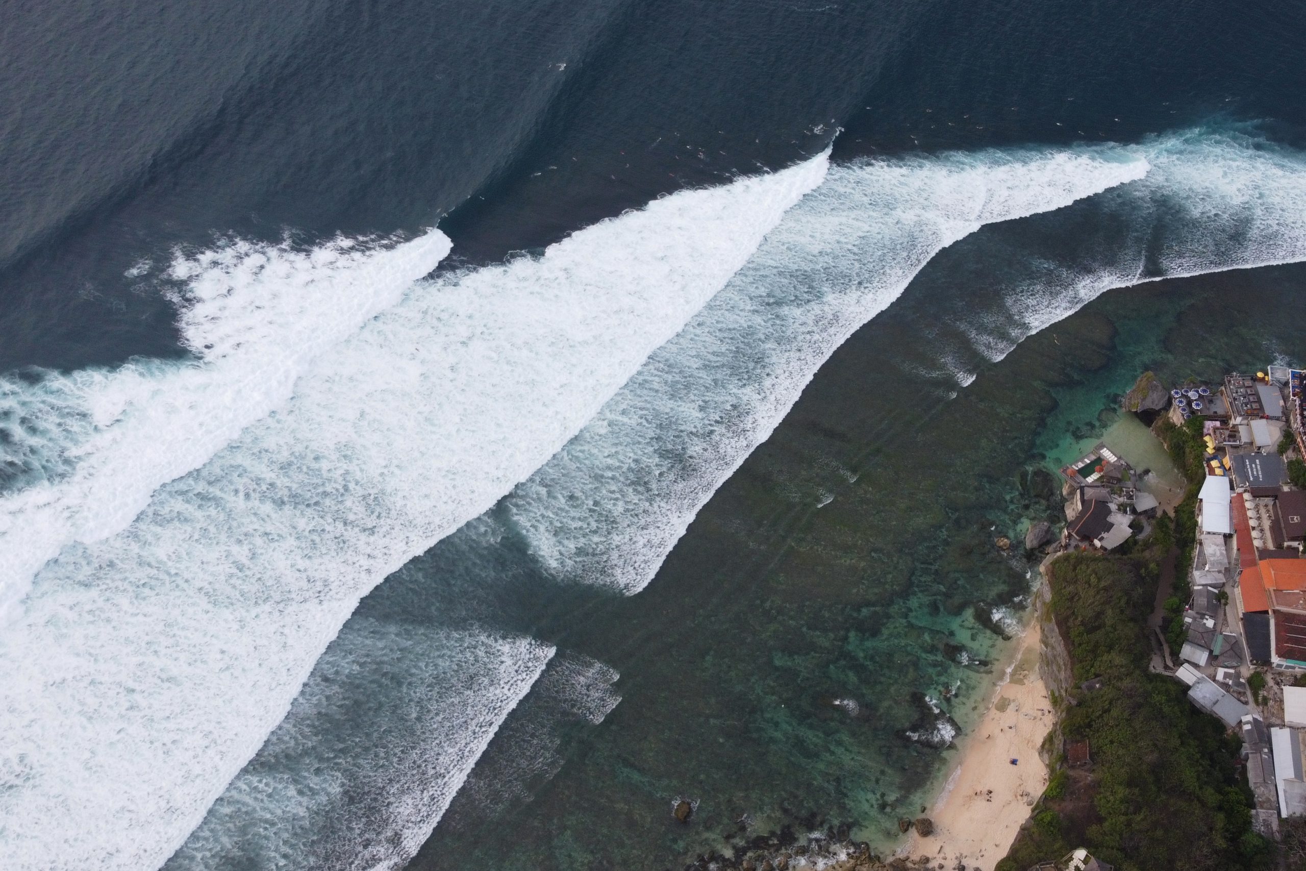 Drohnenaufnahme des legendären Surfspots Uluwatu auf Bali mit Blick auf die Riffsektionen The Peak und Racetrack sowie brechende Wellenlinien.