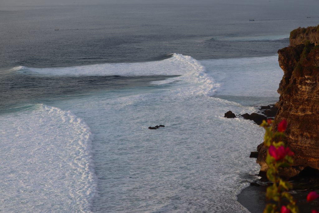 Alternative Text: Steile Klippenküste auf Bali mit Blick auf das schäumende Weisswasser und anrollende Wellen des Ozeans.